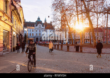Ljubljana, Slovenia - January 15, 2019: Philharmonic hall on Congress Square and cityscape of Ljubljana old town street, Slovenia in evening. Man on bicycle in Slovenian city view in winter. Sunset Stock Photo