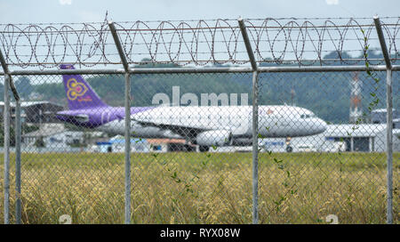 Phuket, Thailand - Apr 23, 2018. Fence with barbed wire around airport with a docking airplane in Phuket International Airport (HKT). Stock Photo