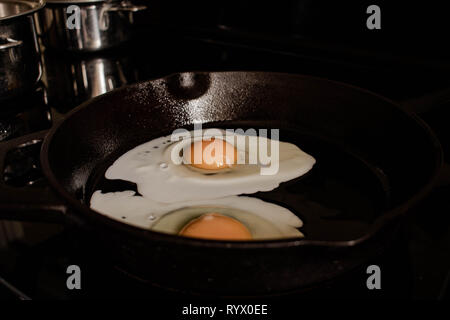 Sunny side up eggs being fried on a cast iron frying pan Stock Photo
