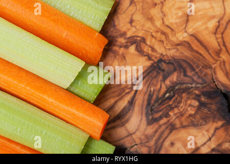 Raw peeled and cut Organic Celery Stalks and Orange Carrots arranged on natural olive wood. Apiaceae or Umbelliferae family. Delicious diet snack. Stock Photo