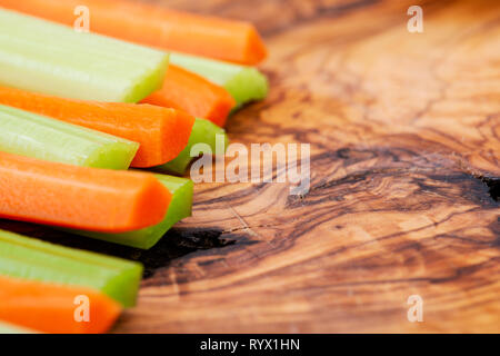 Raw peeled and cut Organic Celery Stalks and Orange Carrots arranged on natural olive wood. Apiaceae or Umbelliferae family. Delicious diet snack. Stock Photo