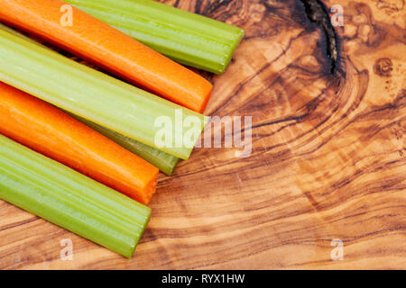 Raw peeled and cut Organic Celery Stalks and Orange Carrots arranged on natural olive wood. Apiaceae or Umbelliferae family. Delicious diet snack. Stock Photo