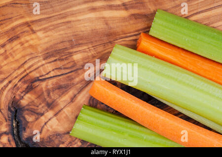 Raw peeled and cut Organic Celery Stalks and Orange Carrots arranged on natural olive wood. Apiaceae or Umbelliferae family. Delicious diet snack. Stock Photo
