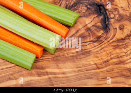 Raw peeled and cut Organic Celery Stalks and Orange Carrots arranged on natural olive wood. Apiaceae or Umbelliferae family. Delicious diet snack. Stock Photo