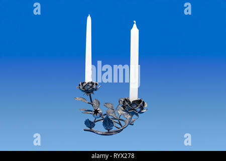 A decorative wrought iron candle holder in the form of two roses with buds and leaves, holding an unlit white candle on an blue isolated background Stock Photo