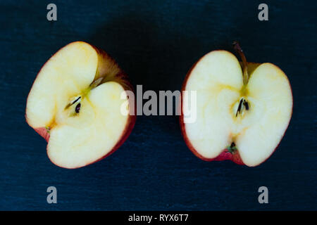 a red apple cut in half on a plain slate background Stock Photo