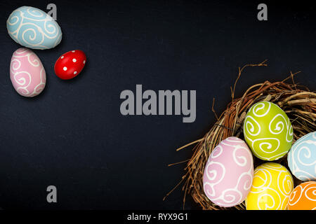 Colorful happy easter eggs in bird nest and tulips on dark empty slate stone blackboard with copy space design pattern Stock Photo