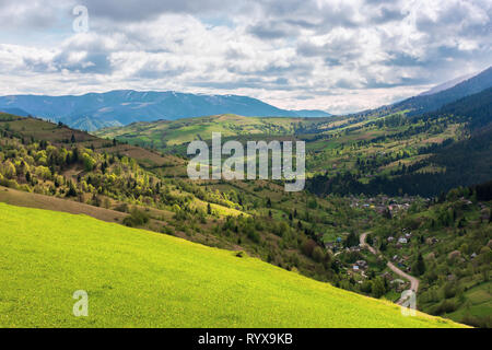 mountainous countryside in springtime. village in the valley, rural fields on hills. distant mountain ridge with spots of snow. sunny weather with clo