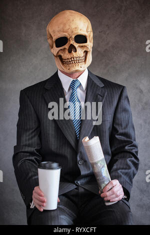 Man in navy blue pinstriped business suit with light blue tie against a gray background wearing a scary human skull mask holding a newspaper and white Stock Photo