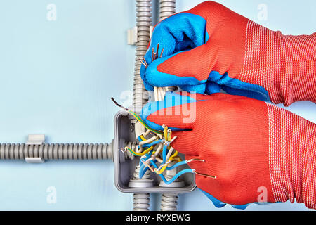 Electrician uses protective gloves to hold wires to twist them together for good contact. Stock Photo