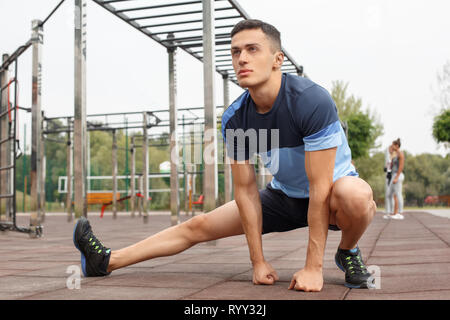 Healthy Lifestyle. Young man doing side squat outdoors looking forward motivated Stock Photo