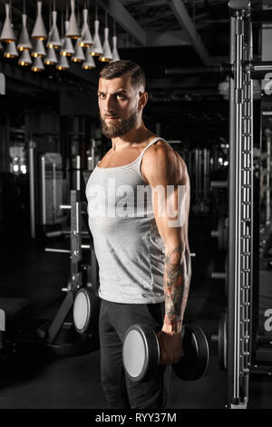 Bodybuilding. Bearded man standing at gym with dumbbells motivated Stock Photo