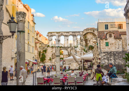 Tourists pass bay a cafe at dusk in the Diocletian's Palace section of the ancient city of Split Croatia with the Silver Gate behind. Stock Photo