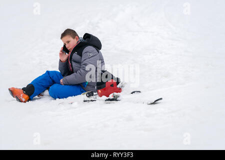 Szklarska Poreba, Poland - February 2019 : Young boy calling for help on his mobile phone after skiing or snowboarding accident on the mountain slope, Stock Photo
