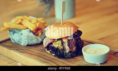 Delicious fresh homemade burger on a wooden table with sauce and French fries. Stock Photo