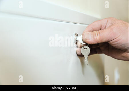 Man's hand is holding and turning a key to open a door. Stock Photo