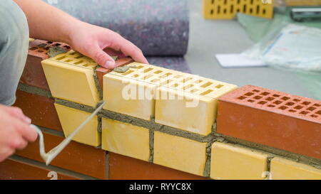 A worker man inserting a small piece of brick in between the big yellow and red bricks with the use of the cement to paste Stock Photo