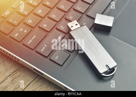 Close up of metal USB flash drive connected to laptop on wood desk Stock Photo