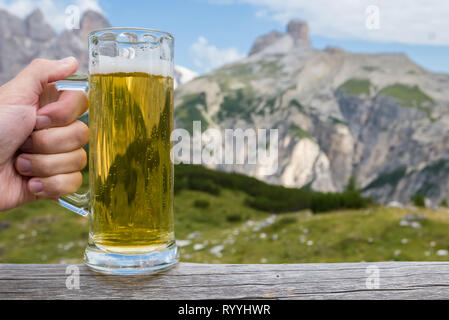 Cold fresh beer, hand holding a mug in alpine mountains Stock Photo