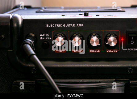 Guitar amplifier with dials and controls for volume, gain, bass, treble. Jack cable connected. Black amp with red light on. Stock Photo