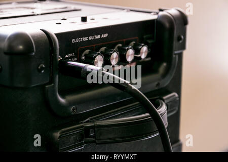 Guitar amplifier with dials and controls for volume, gain, bass, treble. Jack cable connected. Black amp with red light on. Stock Photo