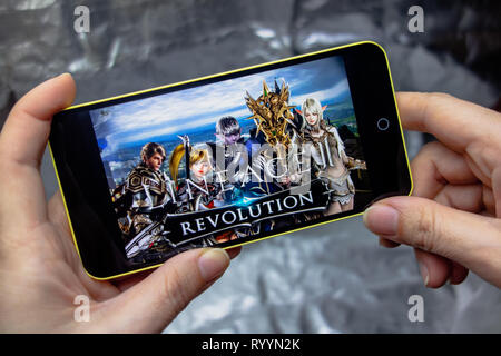 Berdyansk, Ukraine - March 16, 2019: Hands holding a smartphone with lineage 2 revolution game on display screen. Stock Photo