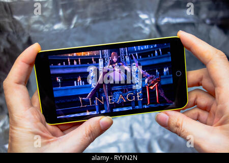 Berdyansk, Ukraine - March 16, 2019: Hands holding a smartphone with lineage 2 revolution game on display screen. Stock Photo