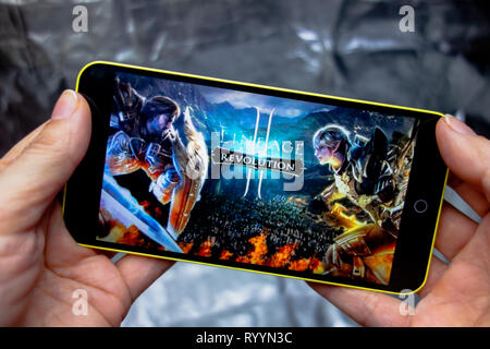 Berdyansk, Ukraine - March 16, 2019: Hands holding a smartphone with lineage 2 revolution game on display screen. Stock Photo