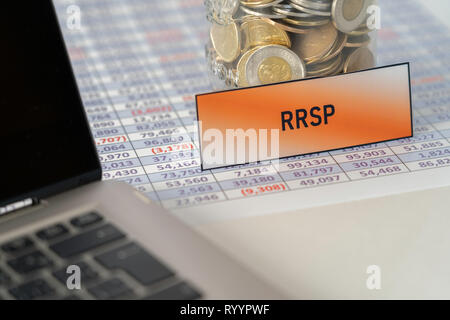 Jar full of Coins for RRSP on spreadsheet next to Laptop Stock Photo