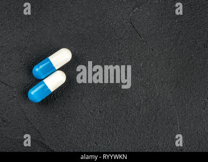 Two white blue capsules on a dark concrete background Stock Photo