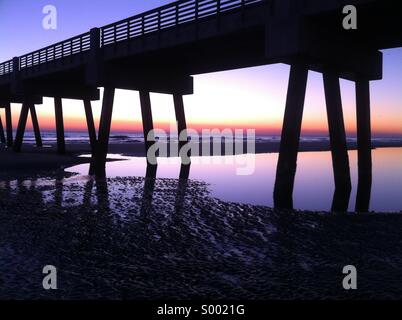 Pooled water reflects a vibrant sunrise sky at Jacksonville Beach Pier in Jacksonville Beach, Florida. USA. Stock Photo