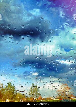 Rainy blue sky and trees seen through wet window Stock Photo