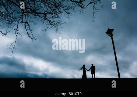 Bride and groom holding hands silhouetted next to a tree and lamppost Stock Photo