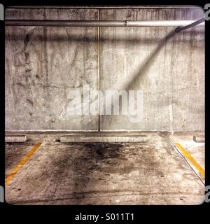 A single shadow cast on a wall in a gritty car park with oil stains on the ground. Stock Photo