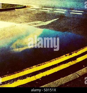 Double yellow lines and reflection of cloud in puddle Stock Photo