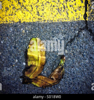 A banana peel that has been run over by a car lying on an asphalt road Stock Photo