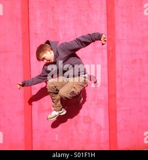 Boy jumping against red wall Stock Photo