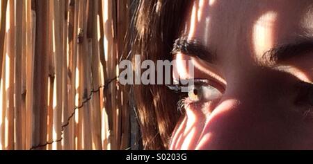 Girl gazes from a bamboo curtain in the striped sunlight. Stock Photo