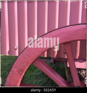 Part of  a cart wheel and siding painted in bright pink Stock Photo