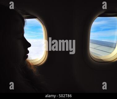 Air travel, teenage girl in profile by window of airplane in flight Stock Photo