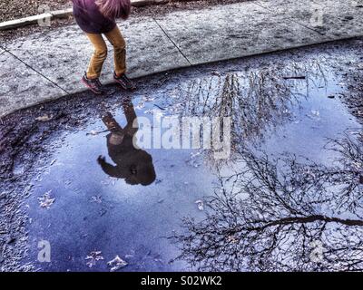 Boy and trees reflected in puddle of water Stock Photo