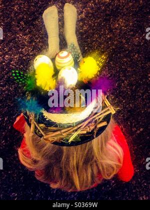 Child sitting on floor wearing home made Easter bonnet Stock Photo