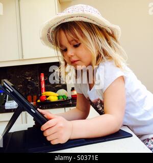 Small girl with a hat on looking at an iPad Stock Photo