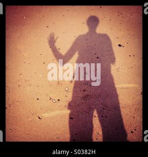 Shadow of a person waving on a sandy beach on the Gower Peninsula, South Wales Stock Photo
