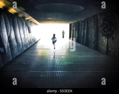 Silhouettes walking through a dark under pass simbolizing light at the end of the tunnel Stock Photo