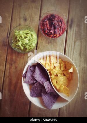 Bowls of blueberry salsa, guacamole, yellow and blue corn chips on picnic  table Stock Photo