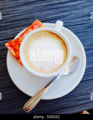 Coffee Cup and sugar packet.white coffee in white cup with spoon on white saucer and orange sugar packet. Stock Photo