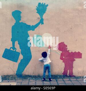 It's a photo of a child who is trying to catch a balloon painted on the wall. It's quite cute and funny Stock Photo