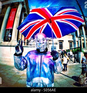 Street performer in Trafalgar Square holding Union Jack umbrella, wearing silver mask Stock Photo