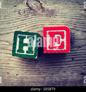 It's a photo of two wood cubes toy with letters that form the word HE Stock Photo